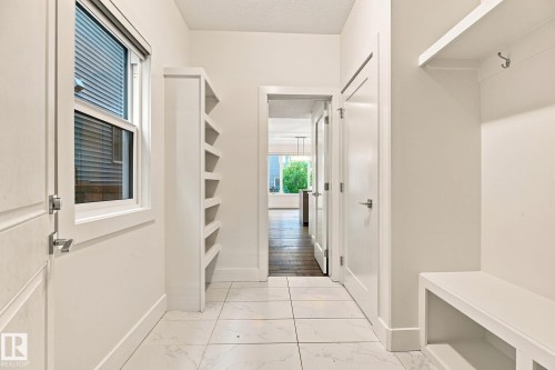 White square tile flooring, built-in shelving, white trim, white window frame, and a built-in bench with coat hooks - 4530 Saly Place Sw, Edmonton, AB 