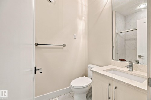 Modern vanity with integrated sink, polished chrome fixtures, frameless mirror, and a glass-enclosed shower with tiled walls - 4530 Saly Place Sw, Edmonton, AB 