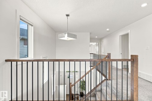 Upper-level landing with wood-finish handrails and black metal balusters - 4530 Saly Place Sw, Edmonton, AB 