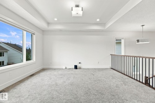 Tray ceiling with recessed lighting and a central light fixture, featuring gray carpeting, white walls, and a large window - 4530 Saly Place Sw, Edmonton, AB 