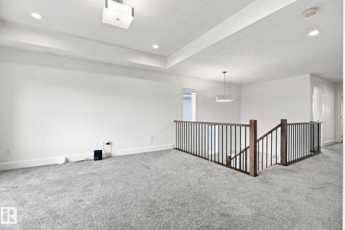 Open loft area with light gray carpeting, recessed ceiling lighting, a modern square flush-mount light fixture, and a contemporary railing system with dark wood posts and black metal balusters - 4530 Saly Place Sw, Edmonton, AB 