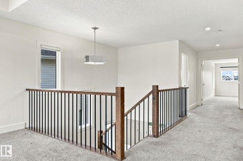 Staircase featuring wood-finish handrails and black metal balusters, recessed lighting, and a contemporary pendant light fixture - 4530 Saly Place Sw, Edmonton, AB 