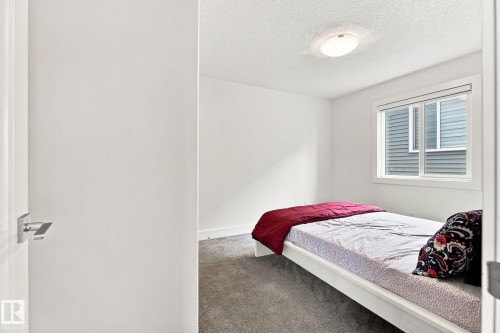 Bedroom featuring a window with blinds, wall-to-wall carpeting, white walls, and a flush-mount ceiling light - 4530 Saly Place Sw, Edmonton, AB 