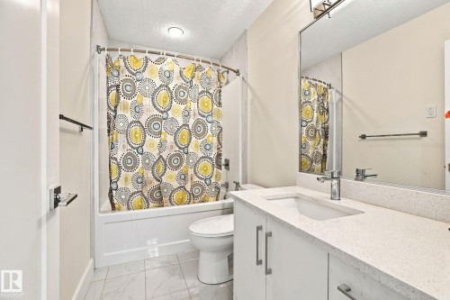 Bathroom featuring a vanity with an integrated sink, polished chrome faucet, and expansive wall-mounted mirror - 4530 Saly Place Sw, Edmonton, AB 