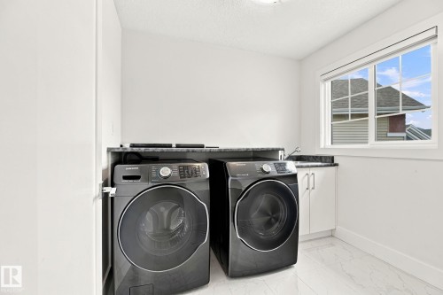 Laundry area featuring a built-in sink, white cabinetry, dark stone-finish countertop, and a window for natural light - 4530 Saly Place Sw, Edmonton, AB 