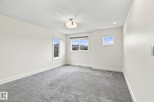 Plush gray carpeting, white painted walls, multiple windows with white trim, a semi-flush mount ceiling light, and a recessed ceiling light - 4530 Saly Place Sw, Edmonton, AB 