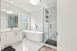 Freestanding soaking tub with floor-mounted faucet, glass-enclosed shower, single vanity with light-toned countertop, large wall-mounted mirror, and tile flooring - 