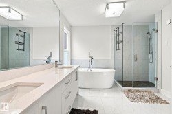 Dual vanity with integrated sinks and white quartz countertops, freestanding soaking tub with floor-mounted faucet, glass-enclosed shower with tiled walls, large format tile flooring, and a full-width wall mirror - 