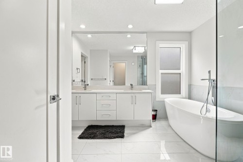 Freestanding soaking tub, dual vanity with undermount sinks, frameless glass shower enclosure, recessed lighting, and large format floor tiles - 4530 Saly Place Sw, Edmonton, AB 