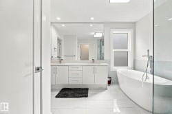 Freestanding soaking tub, dual vanity with undermount sinks, frameless glass shower enclosure, recessed lighting, and large format floor tiles - 