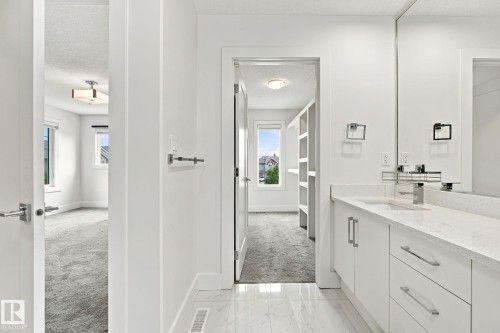White vanity with an integrated sink and brushed nickel faucet, large vanity mirror, white flat-panel cabinetry, and white tile flooring - 4530 Saly Place Sw, Edmonton, AB 