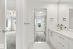 White vanity with an integrated sink and brushed nickel faucet, large vanity mirror, white flat-panel cabinetry, and white tile flooring - 