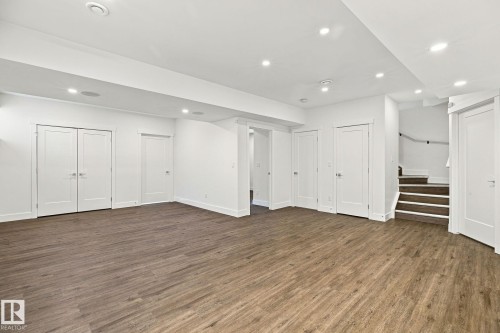 Expansive room featuring wood-finish flooring, recessed lighting, multiple solid panel doors, and a staircase with a handrail - 4530 Saly Place Sw, Edmonton, AB 