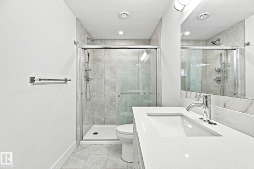 Glass-enclosed shower with tile surround, a built-in vanity with an integrated sink, and a large wall-mounted mirror - 4530 Saly Place Sw, Edmonton, AB 