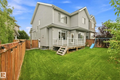 Expansive fenced backyard featuring a wood deck, multiple windows, and light gray siding - 4530 Saly Place Sw, Edmonton, AB 