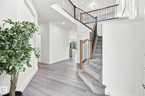 Spacious entry with wood-finish flooring, a carpeted staircase, and a wood and metal railing - 4530 Saly Place Sw, Edmonton, AB 