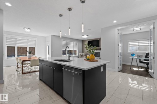 Open-concept living space with large format tile flooring, a kitchen island with integrated sink, pendant lighting, and a separate office space with French doors - 2019 Ware Rd Nw, Edmonton, AB 