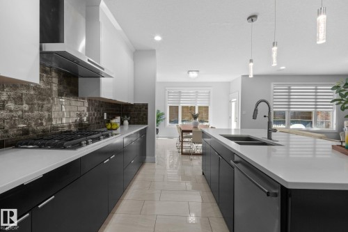 Contemporary kitchen featuring an island with an undermount sink, pendant lighting, matte black cabinetry, light-toned countertops, and a subway tile backsplash - 2019 Ware Rd Nw, Edmonton, AB 
