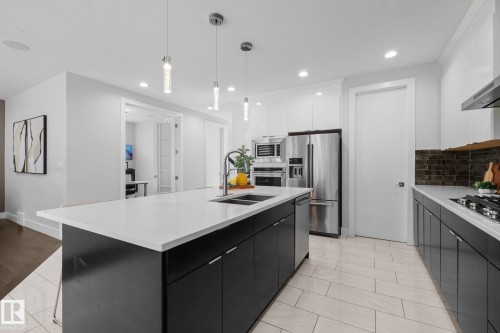 Kitchen featuring a large island with white countertop, dark cabinetry, stainless steel appliances, and ceiling-mounted pendant lights - 2019 Ware Rd Nw, Edmonton, AB 