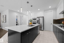 Kitchen featuring a large island with white countertop, dark cabinetry, stainless steel appliances, and ceiling-mounted pendant lights - 