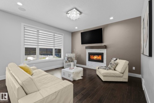 Dark wood-finish flooring with a modern fireplace, white stacked stone surround, and wood mantel - 2019 Ware Rd Nw, Edmonton, AB 