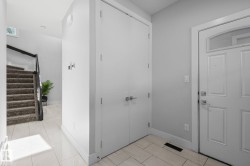 Tiled flooring, white paneled entry door with arched transom, double closet doors with modern hardware, and carpeted stairs with a black handrail - 