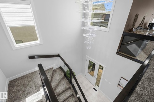 Two-story entryway with a crystal chandelier, wood-finish flooring, and a glass panel railing - 2019 Ware Rd Nw, Edmonton, AB 