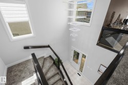 Two-story entryway with a crystal chandelier, wood-finish flooring, and a glass panel railing - 
