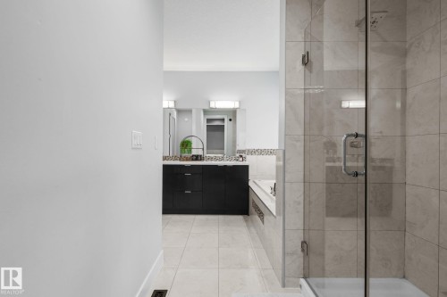 Spacious bathroom featuring a glass-enclosed shower, built-in soaking tub, and a vanity with a stone countertop - 2019 Ware Rd Nw, Edmonton, AB 