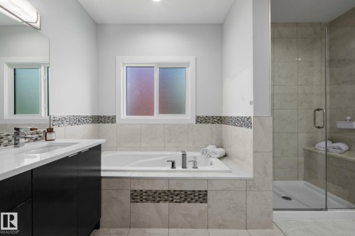 Built-in soaking tub, glass-enclosed shower with tiled bench, dual-sink vanity with dark cabinetry, mosaic tile accents, and tiled walls - 2019 Ware Rd Nw, Edmonton, AB 
