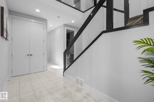 Tiled flooring extending through the entry, contemporary black and glass staircase railing, recessed ceiling lighting, and crisp white walls - 2019 Ware Rd Nw, Edmonton, AB 