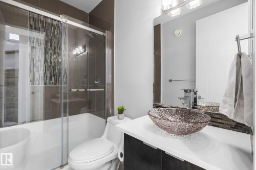 Glass-enclosed shower/tub combination with mosaic tile accent, vessel sink vanity with modern faucet, and large rectangular wall mirror - 2019 Ware Rd Nw, Edmonton, AB 
