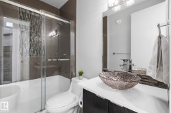 Glass-enclosed shower/tub combination with mosaic tile accent, vessel sink vanity with modern faucet, and large rectangular wall mirror - 