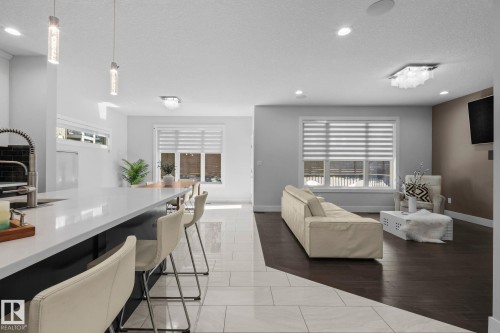 Open-concept living area featuring a large kitchen island with a white countertop, recessed lighting, wood-finish flooring, and a contemporary light fixture - 2019 Ware Rd Nw, Edmonton, AB 