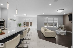 Open-concept living area featuring a large kitchen island with a white countertop, recessed lighting, wood-finish flooring, and a contemporary light fixture - 