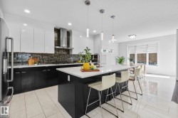 Modern kitchen featuring stainless steel appliances, a center island with countertop seating, dark cabinetry, and a subway tile backsplash - 