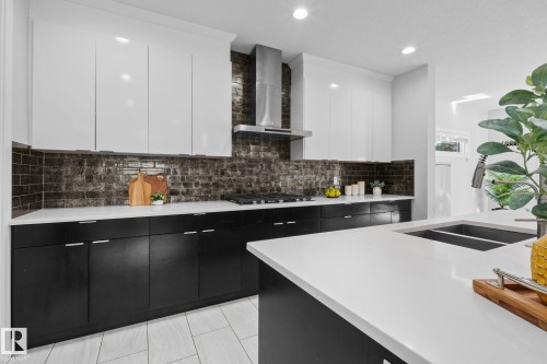 Modern kitchen featuring white upper cabinetry, dark lower cabinetry, white countertops, a dark subway tile backsplash, and a stainless steel range hood - 2019 Ware Rd Nw, Edmonton, AB 