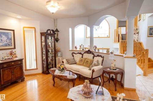 Open concept living area featuring wood-finish flooring, architectural arches, and a prominent staircase with wood railings - 6407 163 Avenue Nw, Edmonton, AB 