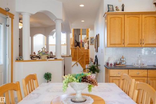 Open-concept dining area featuring a wood table with chair seating, wood cabinetry, light tile backsplash, and dark countertops - 6407 163 Avenue Nw, Edmonton, AB 