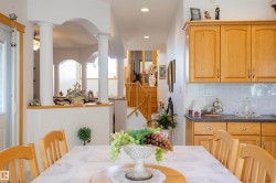 Open-concept dining area featuring a wood table with chair seating, wood cabinetry, light tile backsplash, and dark countertops - 