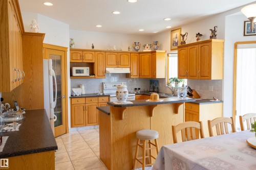 Kitchen featuring light wood cabinetry, dark countertops, a tiled backsplash, recessed lighting, and a breakfast bar - 6407 163 Avenue Nw, Edmonton, AB 