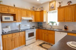 Kitchen featuring abundant wood-finish cabinetry, solid surface countertops, white tile backsplash, and a double basin sink beneath a bay window - 