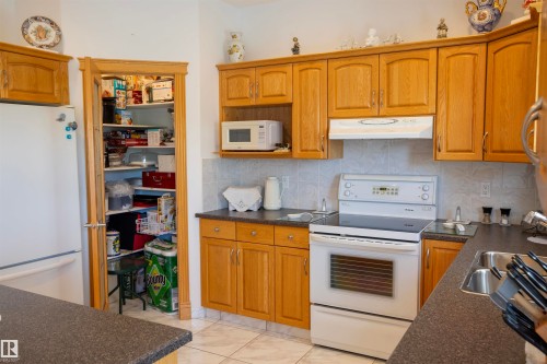 Kitchen featuring wood-finish cabinetry, white appliances, and a tiled backsplash - 6407 163 Avenue Nw, Edmonton, AB 