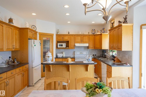 Spacious kitchen featuring light wood cabinetry, dark countertops, white tile backsplash, a central island with breakfast bar seating, and recessed lighting - 6407 163 Avenue Nw, Edmonton, AB 