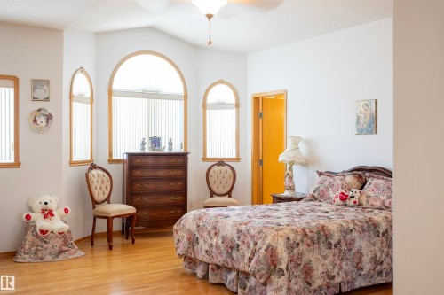 Interior space featuring a vaulted ceiling with a ceiling fan, multiple arched windows with wood trim, wood-finish flooring, and a solid-core door - 6407 163 Avenue Nw, Edmonton, AB 