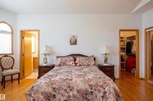 Bedroom featuring light wood-finish flooring, an arched window with blinds, a doorway to a bathroom with a vanity, and a doorway to a closet with built-in shelving - 6407 163 Avenue Nw, Edmonton, AB 