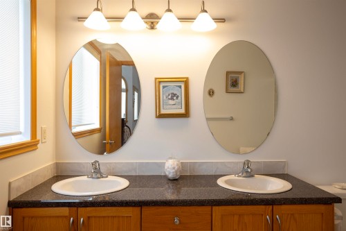 Double vanity featuring two oval mirrors, a dark countertop, and wood-finish cabinetry - 6407 163 Avenue Nw, Edmonton, AB 