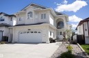 Two-story stucco exterior featuring an arched entryway with decorative transom window, an attached two-car garage with sunburst window detailing, and a concrete driveway - 6407 163 Avenue Nw, Edmonton, AB 