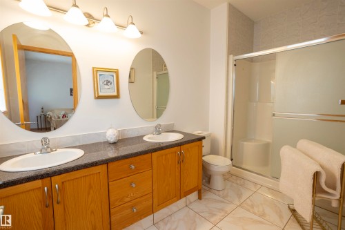 Bathroom featuring a dual vanity with wood cabinetry, dark speckled countertops, and oval mirrors - 6407 163 Avenue Nw, Edmonton, AB 