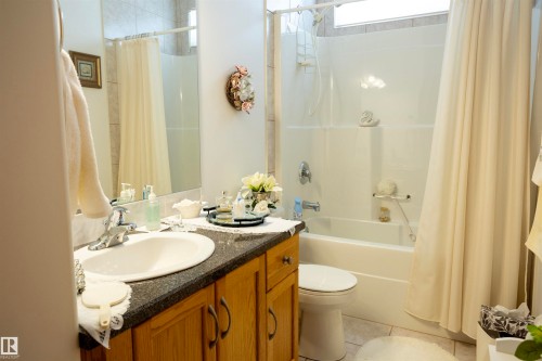 Bathroom featuring a full-size bathtub with an overhead shower, a single vanity with a dark countertop, wood-finish cabinetry, and an integrated basin - 6407 163 Avenue Nw, Edmonton, AB 